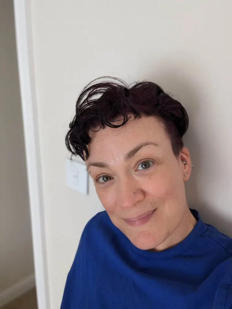Kate smiling, with short dark curly hair and a blue top.