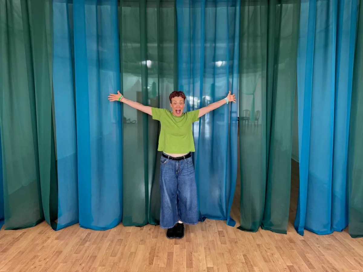 Kate stands between blue voile curtains with her arms flung wide, as if saying ta-da.