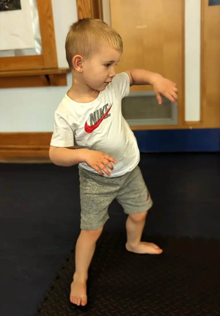A barefoot boy makes a shape with his arms and legs.